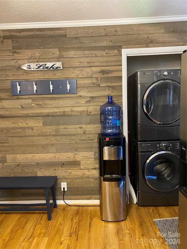 clothes washing area featuring hardwood / wood-style floors, stacked washer / drying machine, crown molding, and wood walls