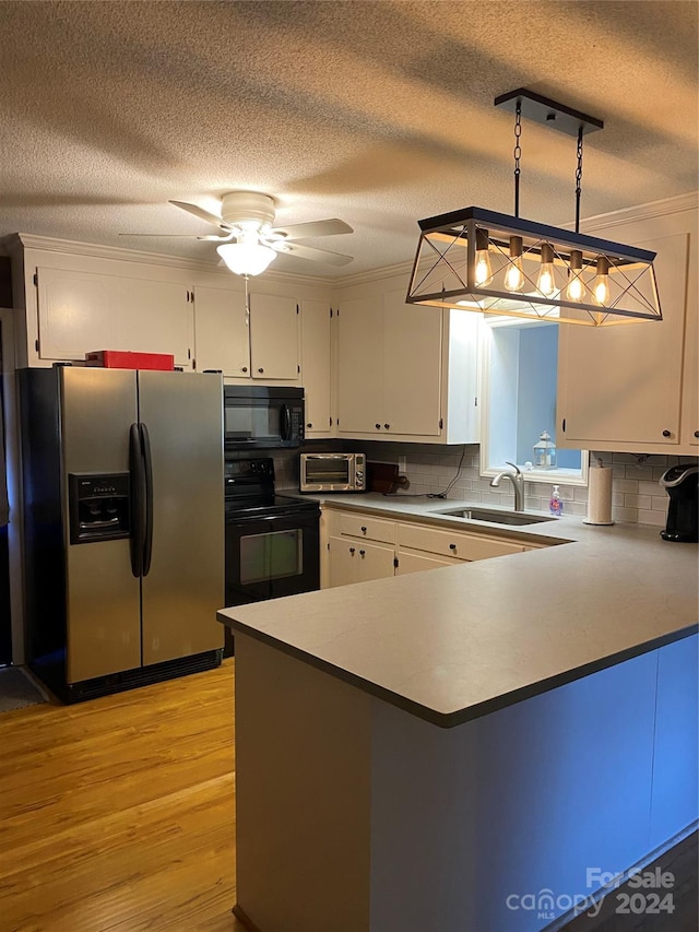 kitchen with sink, black appliances, white cabinets, and hanging light fixtures