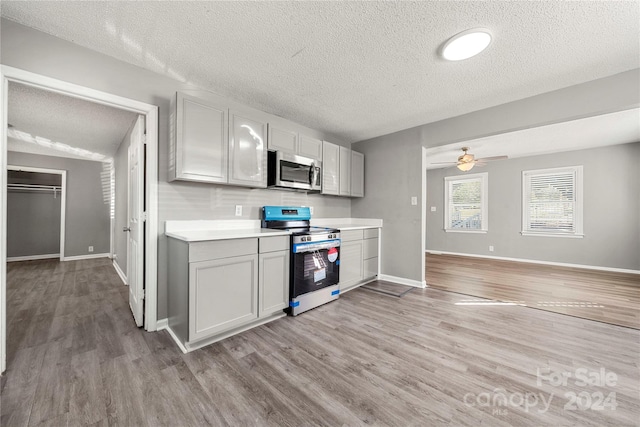 kitchen with gray cabinetry, ceiling fan, stove, light wood-type flooring, and a textured ceiling