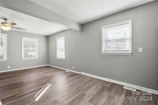 empty room with ceiling fan, a textured ceiling, beam ceiling, and hardwood / wood-style floors