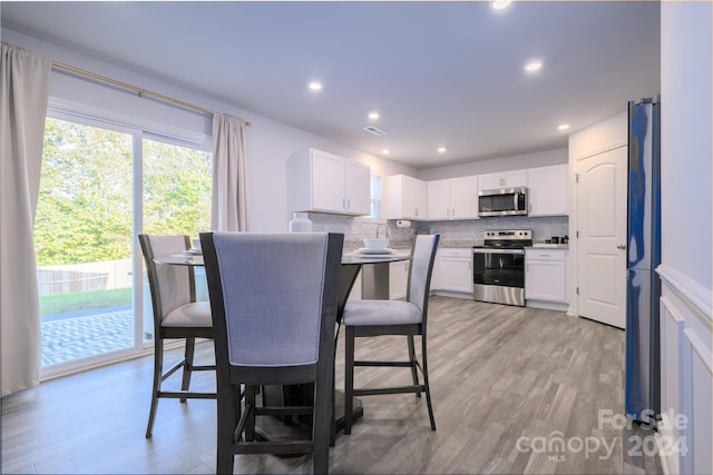 kitchen with backsplash, white cabinetry, light hardwood / wood-style flooring, and appliances with stainless steel finishes