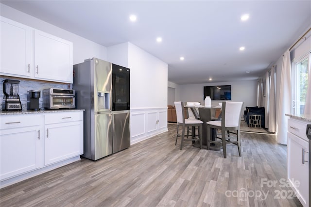 kitchen with white cabinetry, stainless steel fridge, light hardwood / wood-style flooring, and light stone counters