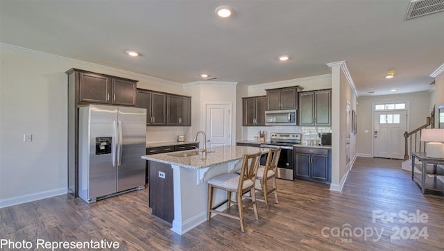 kitchen with a center island with sink, dark hardwood / wood-style floors, appliances with stainless steel finishes, and light stone countertops