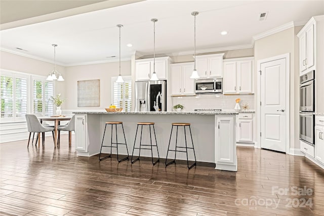 kitchen with stainless steel appliances, light stone counters, white cabinets, an island with sink, and decorative light fixtures