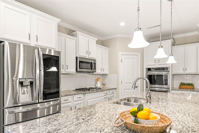 kitchen with light stone counters, appliances with stainless steel finishes, decorative light fixtures, sink, and white cabinets