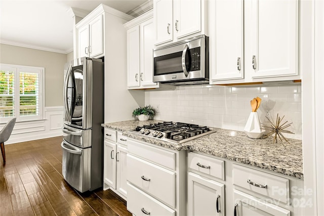 kitchen with light stone counters, ornamental molding, white cabinetry, appliances with stainless steel finishes, and dark hardwood / wood-style flooring