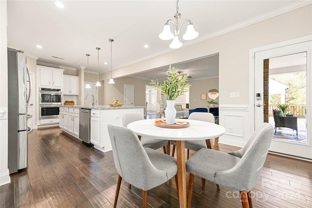 dining area featuring dark wood-type flooring, a chandelier, sink, and crown molding