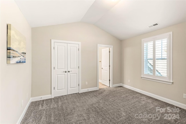 unfurnished bedroom with a closet, lofted ceiling, carpet flooring, and ensuite bath