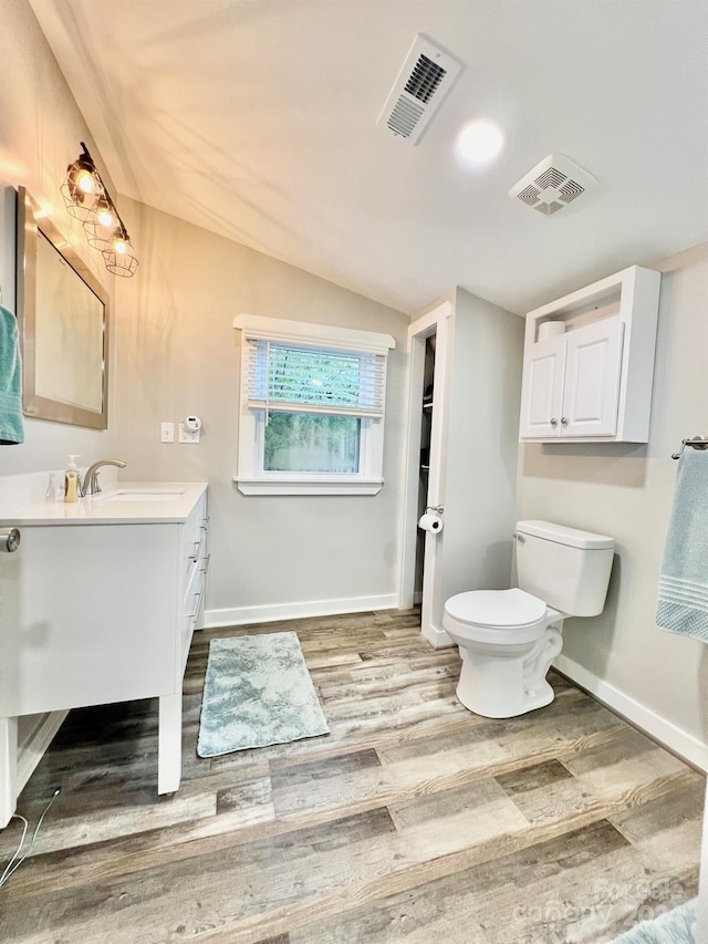 bathroom with hardwood / wood-style floors, vanity, toilet, and vaulted ceiling