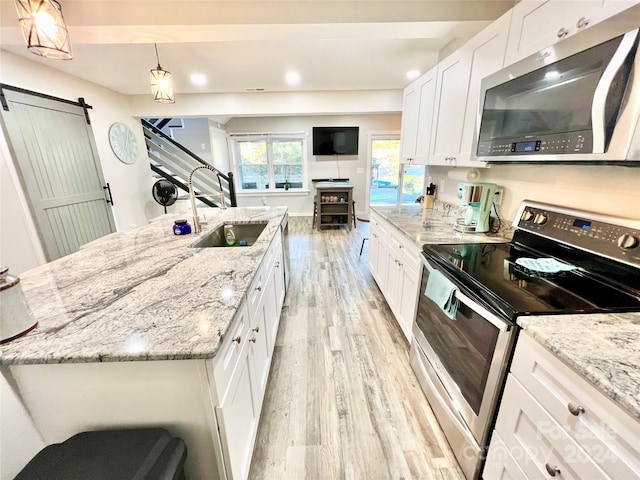 kitchen featuring appliances with stainless steel finishes, a barn door, sink, light hardwood / wood-style floors, and white cabinets