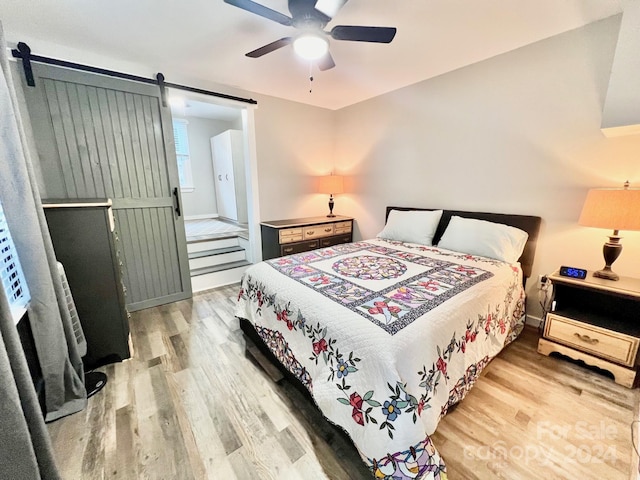 bedroom with wood-type flooring, a barn door, and ceiling fan