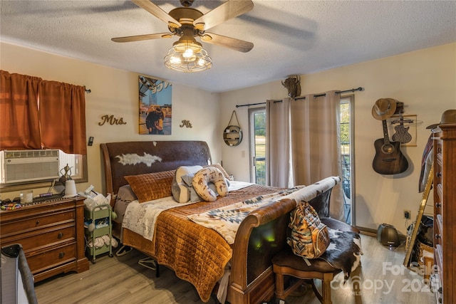 bedroom with light wood-type flooring, cooling unit, a textured ceiling, and ceiling fan