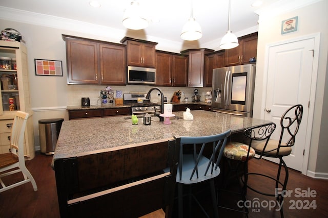 kitchen with a kitchen island with sink, dark wood-type flooring, ornamental molding, light stone countertops, and appliances with stainless steel finishes