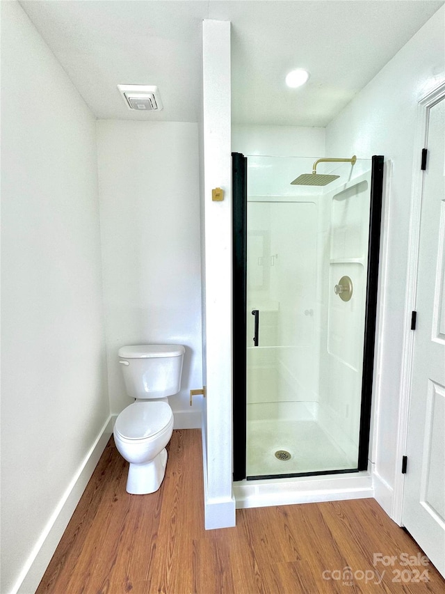 bathroom with wood-type flooring, a shower with door, and toilet