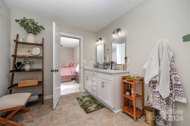ensuite bathroom featuring stone finish flooring, a textured ceiling, vanity, baseboards, and ensuite bath