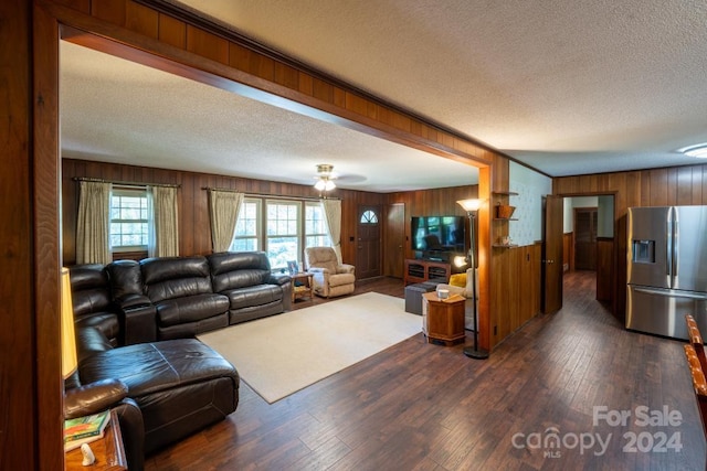 living room with wood walls, a textured ceiling, ceiling fan, and dark hardwood / wood-style flooring