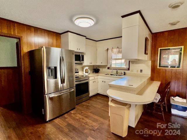 kitchen featuring white cabinetry, stainless steel appliances, wooden walls, and dark hardwood / wood-style floors