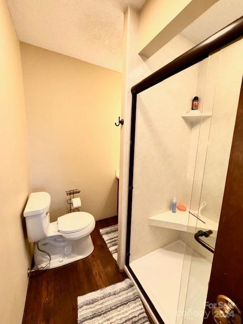 bathroom with toilet, a textured ceiling, wood-type flooring, and a shower with door