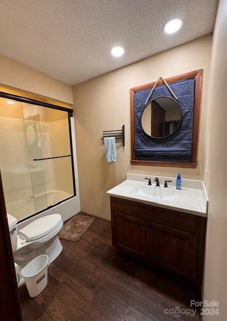 full bathroom with bath / shower combo with glass door, a textured ceiling, wood-type flooring, toilet, and vanity