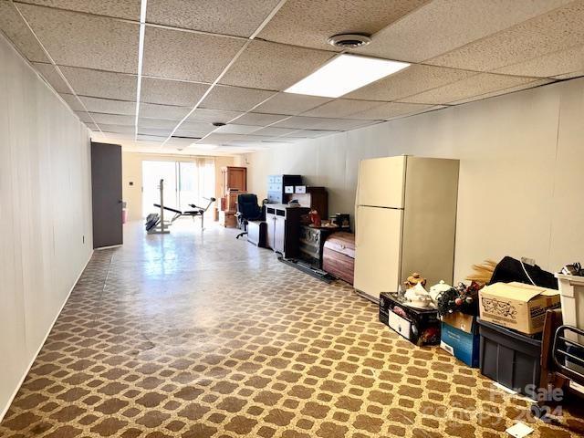 basement with a paneled ceiling and white fridge