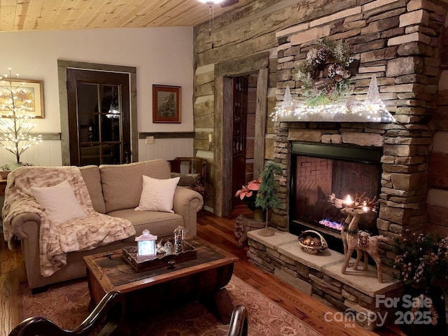 living room with wood ceiling, vaulted ceiling, a stone fireplace, and wood-type flooring