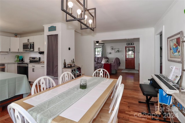 dining area featuring ornamental molding, dark wood-type flooring, and ceiling fan with notable chandelier