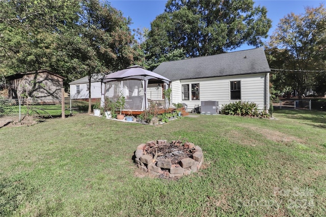 back of property featuring central air condition unit, an outdoor fire pit, a lawn, a gazebo, and a shed