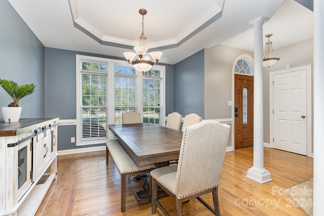 dining room with decorative columns, a tray ceiling, crown molding, light hardwood / wood-style flooring, and an inviting chandelier