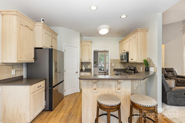 kitchen featuring backsplash, kitchen peninsula, light hardwood / wood-style floors, stainless steel appliances, and a breakfast bar