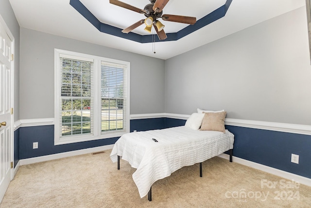 bedroom featuring a raised ceiling, light colored carpet, and ceiling fan