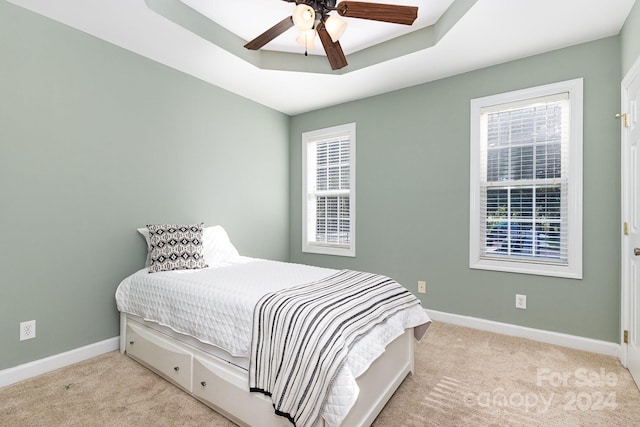 bedroom featuring light colored carpet, a tray ceiling, and ceiling fan