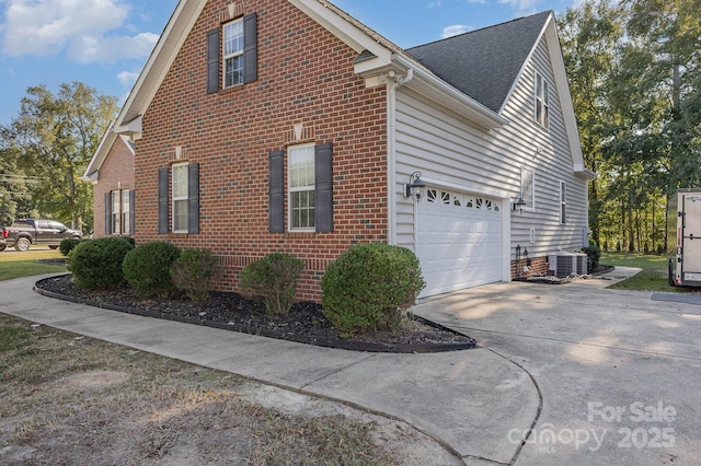 view of home's exterior with a garage, concrete driveway, roof with shingles, central air condition unit, and brick siding