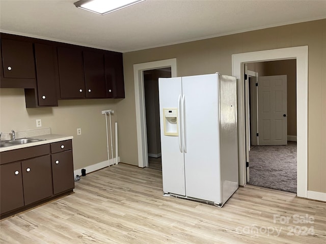 kitchen with dark brown cabinets, white refrigerator with ice dispenser, light hardwood / wood-style floors, and sink