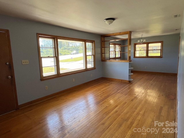 unfurnished living room with an inviting chandelier and light hardwood / wood-style flooring