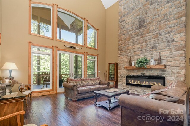 living room featuring a stone fireplace, a high ceiling, and dark hardwood / wood-style floors