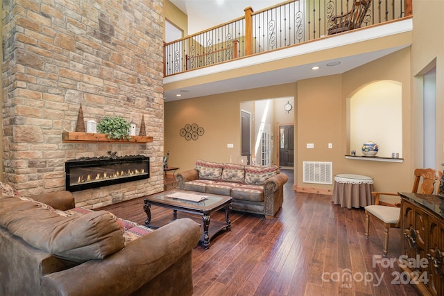 living room featuring dark wood-type flooring, a stone fireplace, and a towering ceiling