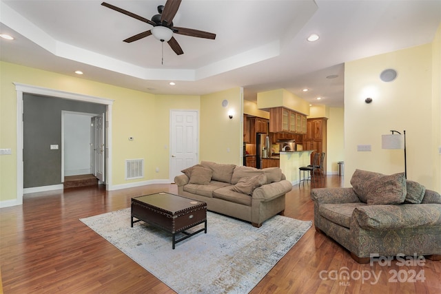 living room with ceiling fan, a tray ceiling, and dark hardwood / wood-style flooring