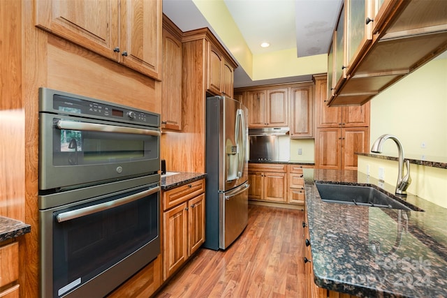 kitchen with dark stone counters, stainless steel appliances, sink, and light wood-type flooring