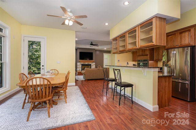 dining room featuring a stone fireplace, ceiling fan, and dark hardwood / wood-style flooring