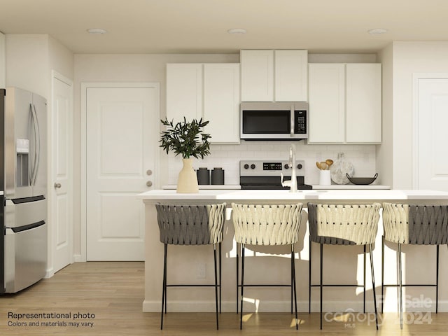 kitchen featuring a breakfast bar, white cabinets, stainless steel appliances, and light hardwood / wood-style floors