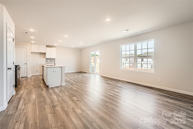 unfurnished living room with a sink, recessed lighting, baseboards, wood finished floors, and visible vents