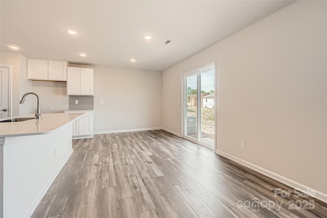 kitchen featuring a sink, light countertops, light wood finished floors, recessed lighting, and white cabinetry