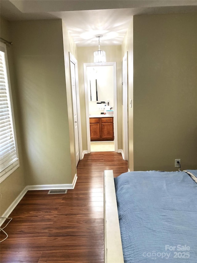 unfurnished bedroom featuring connected bathroom, a notable chandelier, and dark hardwood / wood-style floors