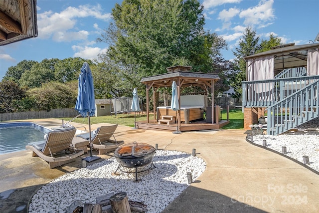 view of patio featuring a gazebo, a fire pit, a storage shed, and a swimming pool with hot tub