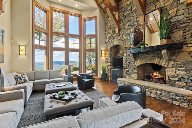 living room featuring a stone fireplace, hardwood / wood-style flooring, a towering ceiling, and beamed ceiling