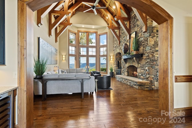 living room with beam ceiling, a stone fireplace, beverage cooler, dark wood-type flooring, and high vaulted ceiling