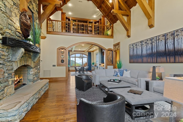 living room with a stone fireplace, hardwood / wood-style flooring, beamed ceiling, and high vaulted ceiling