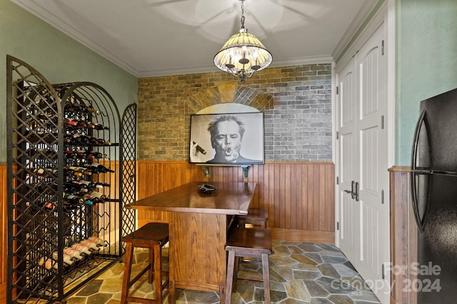 wine room featuring ornamental molding, wooden walls, an inviting chandelier, and brick wall