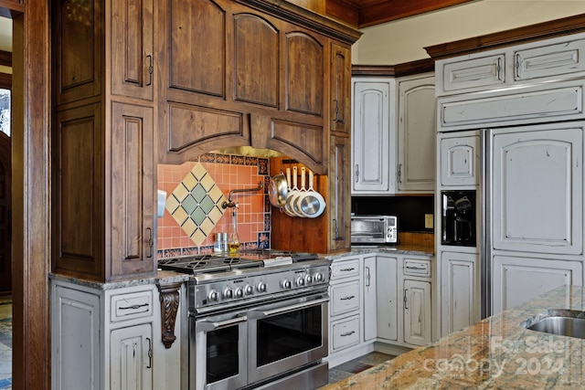 kitchen with light stone countertops, backsplash, high end appliances, and white cabinetry