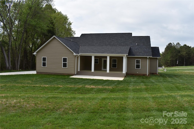 back of house featuring roof with shingles, a lawn, and covered porch